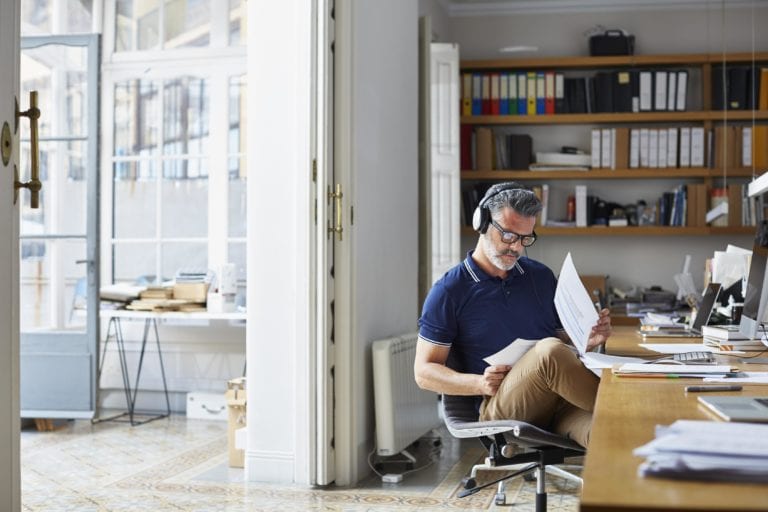 Man wearing headphones looking through papers at desk.